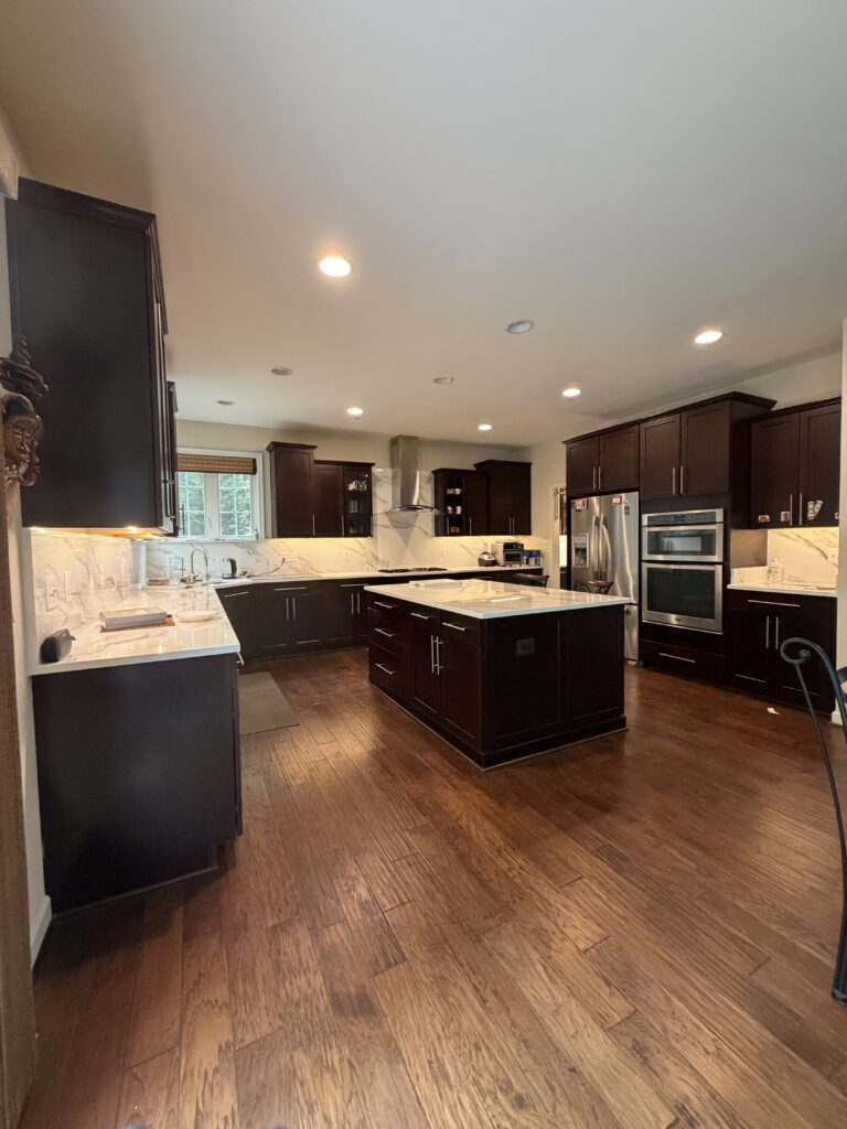 Under-cabinet LED lighting illuminating white countertops and backsplash in a kitchen with dark wood cabinets.