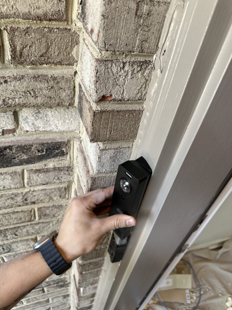 Technician fitting a video doorbell beside a brick doorway.