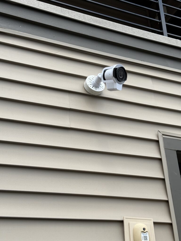 Outdoor security camera mounted on exterior siding beneath a window.