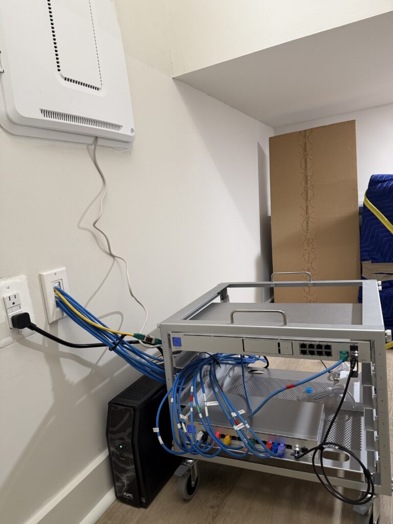 Network equipment rack with a patch panel, connected Ethernet cables and wall-mounted data outlets.