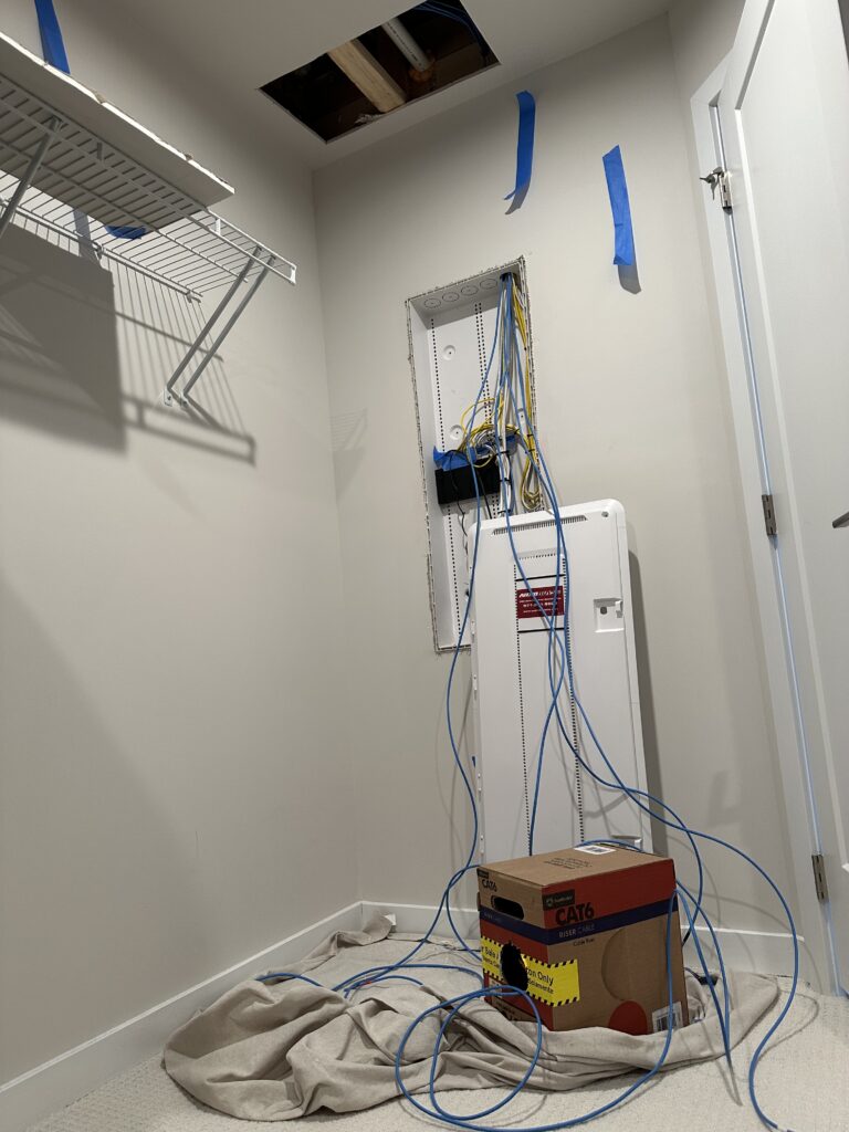 Network installation in progress with exposed wall openings, Ethernet cables and a structured media enclosure.