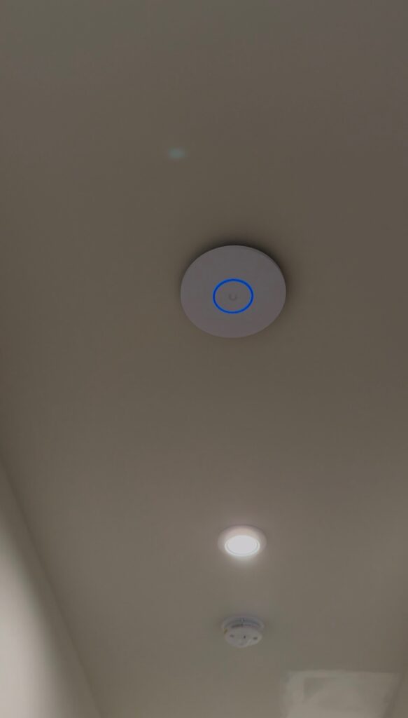 Close-up of a ceiling-mounted wireless access point U6 Pro with a blue illuminated status ring.